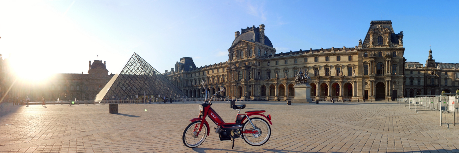 Une mobylette rouge devant la pyramide du Louvre