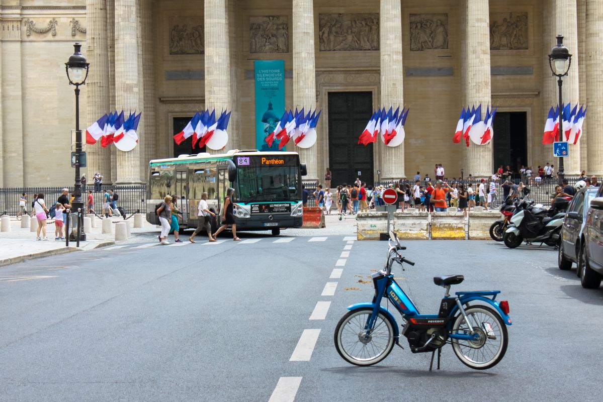 Une mobylette devant le Panthéon couvert de drapeaux français.