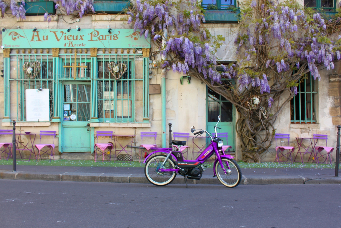 Une mobylette devant un café parisien avec une façade couverte de fleur