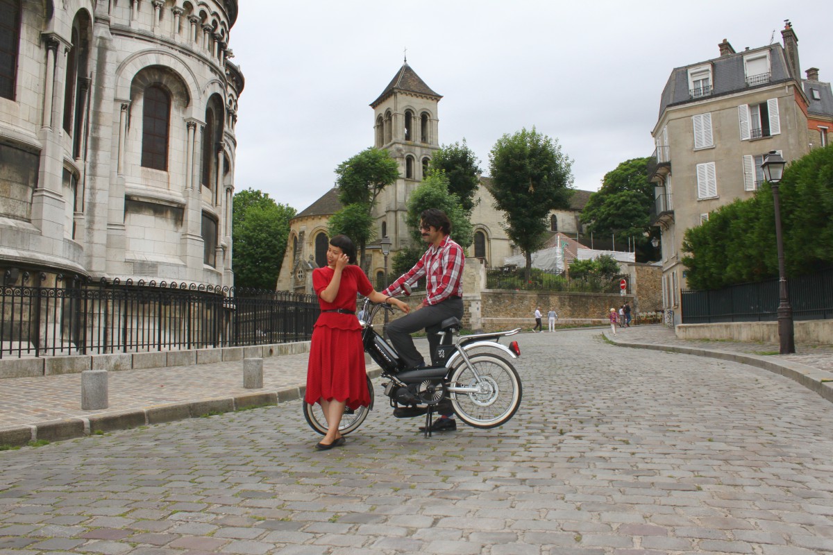 Un couple avec des habits vintage sur une mobylette dans une rue de Montmartre