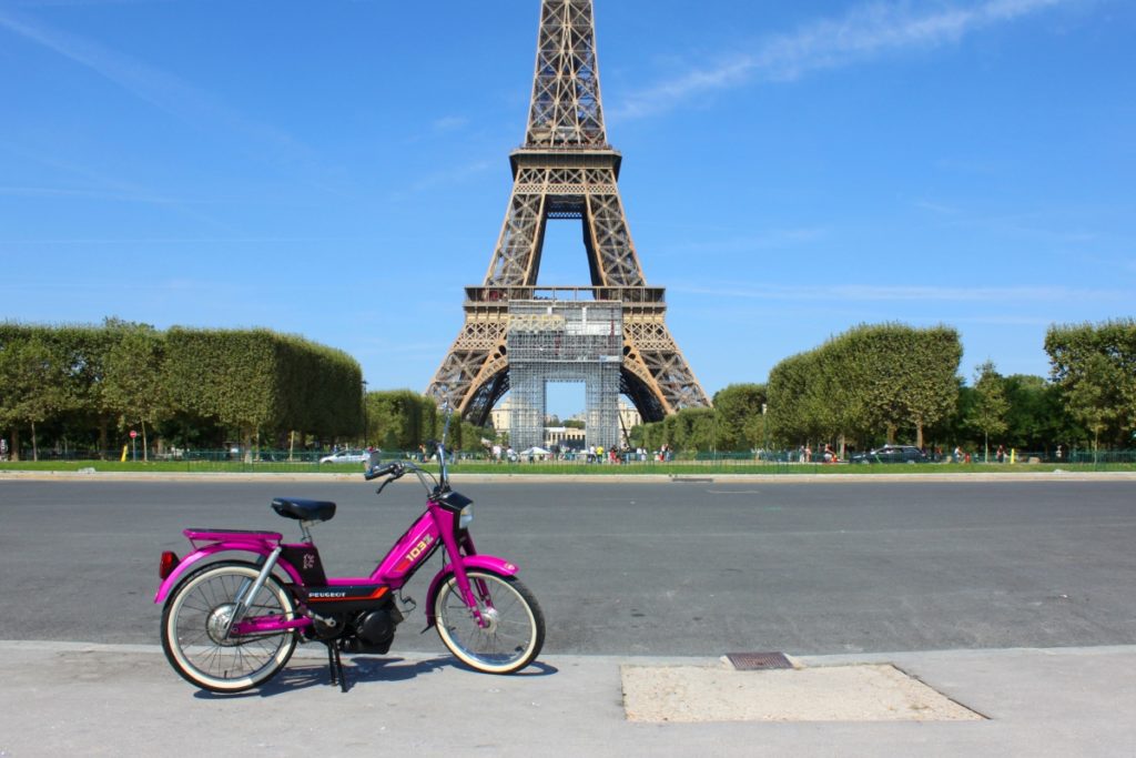 Une mobylette rose devant la Tour Eiffel