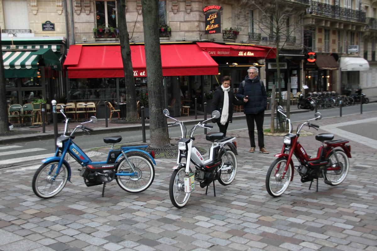 Un couple regardant trois mobylettes sur une place parisienne